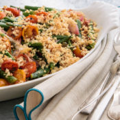 A plate of Curtis Stone's Green Bean and Tomato Gratin next to silverware.