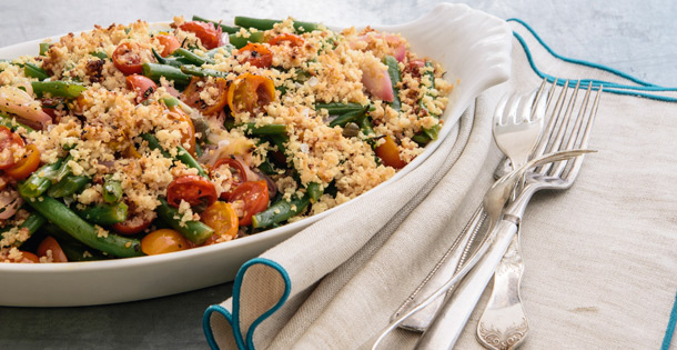 A plate of Curtis Stone's Green Bean and Tomato Gratin next to silverware.