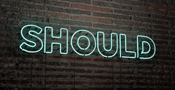 Neon sign that reads "Should" on a brick wall.