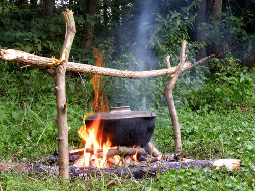 A cooking pot is suspended over a buring campfire with branches