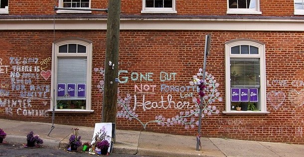 A memorial on a brick wall next to a street in Charlottesville. Graffiti is written on it, saying "Gone But Not Forgotten Heather".