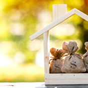 Small bags of money in a wooden frame shaped like a house, symbolizing investing into a home.