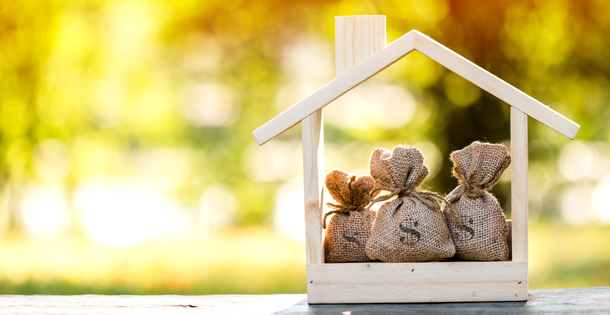 Small bags of money in a wooden frame shaped like a house, symbolizing investing into a home.