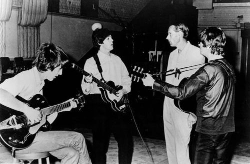Beatles members George Harrison, Paul McCartney, and John Lennon with instruments confering with producer George Martin