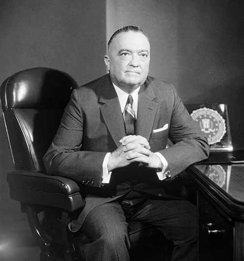 J. Edgar Hoover sits in a chair with folded hands