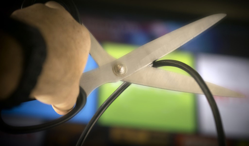 A man cutting a coaxial cable wire, siginifying canceling cable TV service.