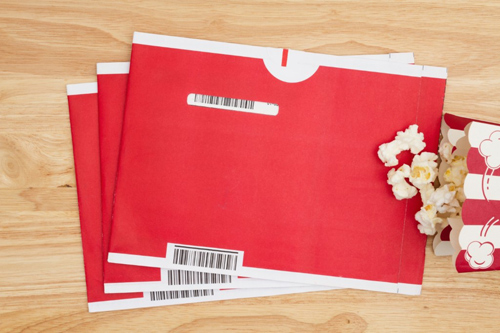 Several Netflix DVD envelopes on a table next to some popcorn.