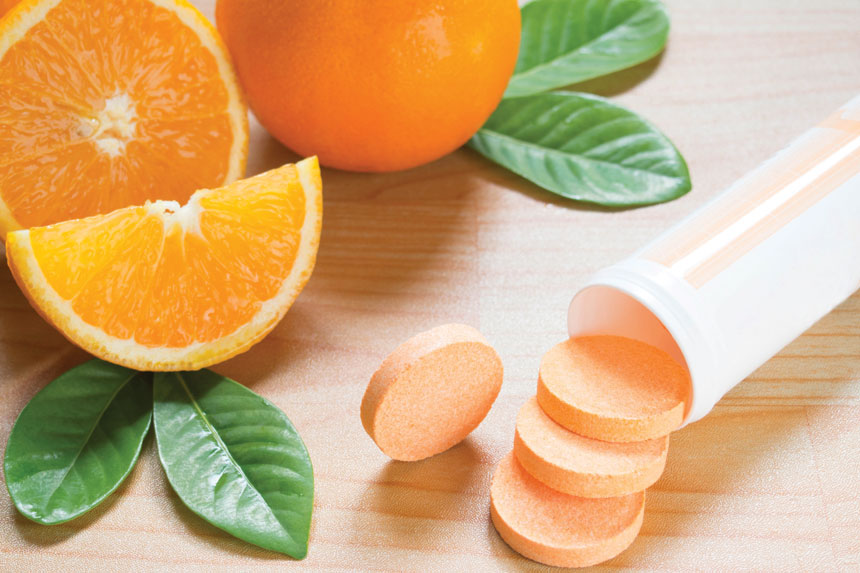 Vitamin C tablets on a wooden surface with sliced oranges