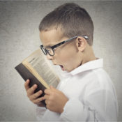 A young boy with glasses screaming into an open book