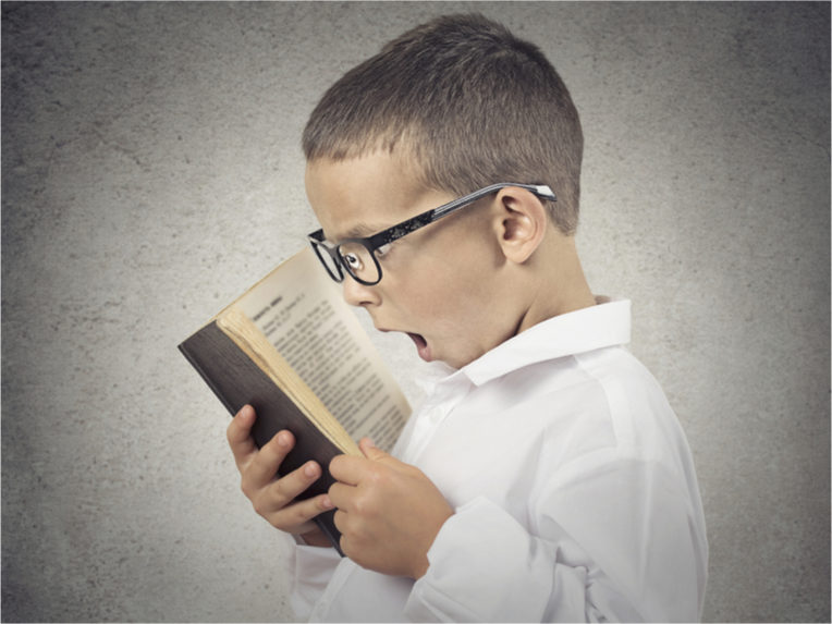 A young boy with glasses screaming into an open book