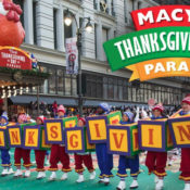 People in elf costumes holding letter blocks that spell "Thanksgiving" during the Macy's Thanksgivng Parade