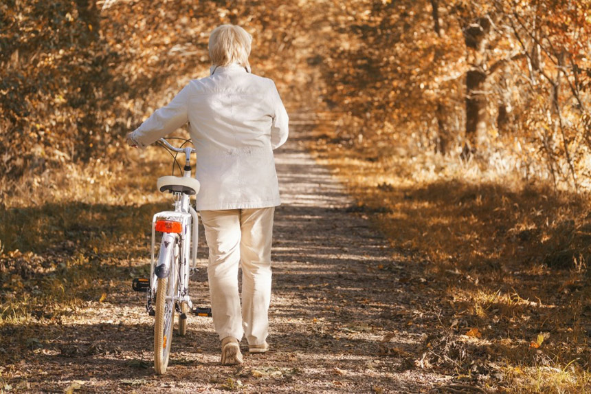 Woman walking her bike down a woody path full of autumn leaves