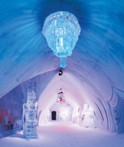 A room in an ice hotel, with statues, chairs, and a chandelier carved from ice.