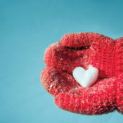 Someone holding a heart-shaped snow sculpture with a pair of wool mittens.