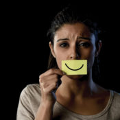 Unhappy woman holding a post-it note with a smiley face over her mouth.
