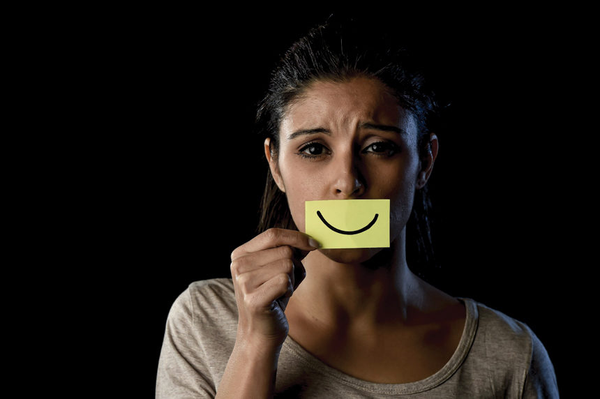 Unhappy woman holding a post-it note with a smiley face over her mouth.