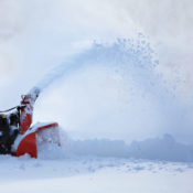 A man using a snowblower to remove snow from a driveway.