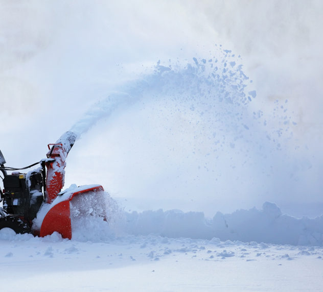 A man using a snowblower to remove snow from a driveway.