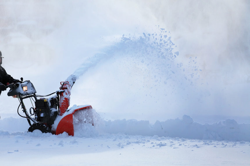 A man using a snowblower to remove snow from a driveway.