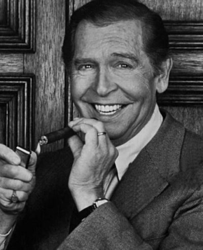 Comedian Milton Berle smiling and liting a cigar