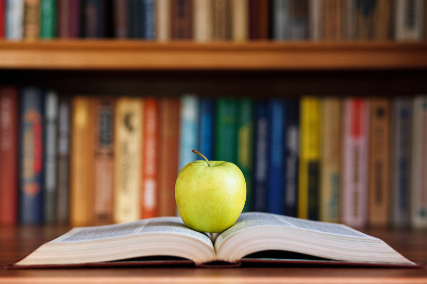 A tart apple resting on an open book in the middle of a library