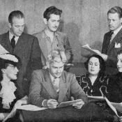 Soap opera cast members crowd around a table during a script reading.