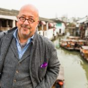 Andrew Zimmern stands in front of a city river