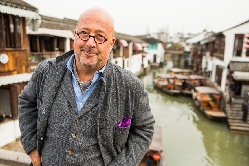 Andrew Zimmern stands in front of a city river