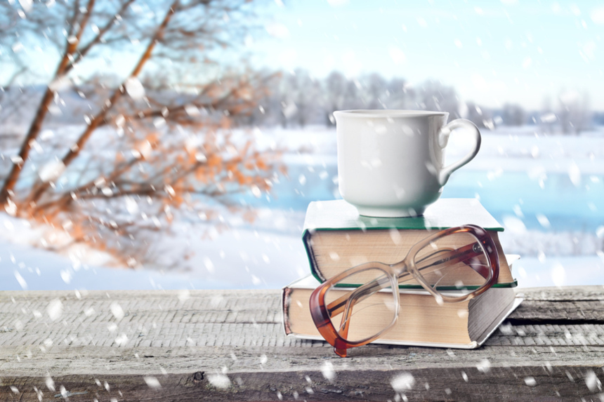 A coffee mug resting on a pile of books outside on a table during snowfall.