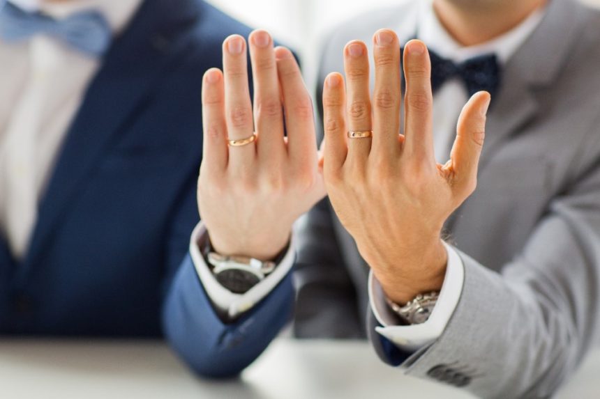 A gay couple holding up their wedding bands.