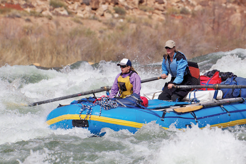 Two women rafting down rapid water in the Colorado River, rushing through the Grand Canyon.