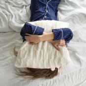 A woman in pajamas places a pillow on her head, refusing to get out of bed.