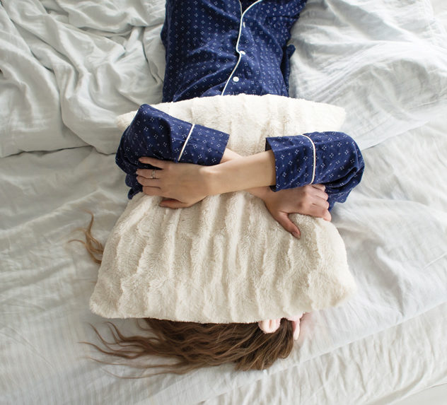 A woman in pajamas places a pillow on her head, refusing to get out of bed.