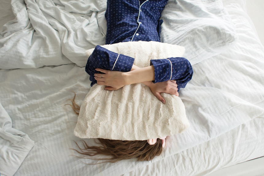 A woman in pajamas places a pillow on her head, refusing to get out of bed.