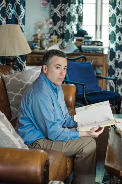 Michael Frank holds a copy of his insurance policy in his living room.