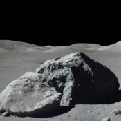 An astronaut next to a giant rock on the moon.