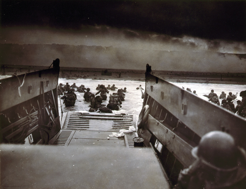 U.S. and British soldiers disembark their landing boats into the shallow waters of the Normandy shore, braving heavy machine gun fire and sniper bullets.