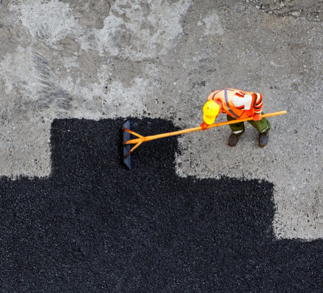 Construction worker laying down asphalt over an old road