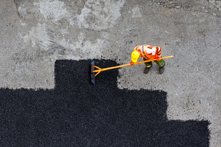 Construction worker laying down asphalt over an old road