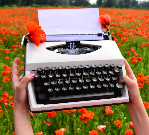 Woman holding a typewriter in a flower field