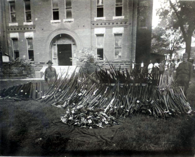 Longview, TX police officers stand next to a pile of rifles and ammunition left by the town's white residents, who left the weapons in front of the courthouse to terrorize their black neighbors.