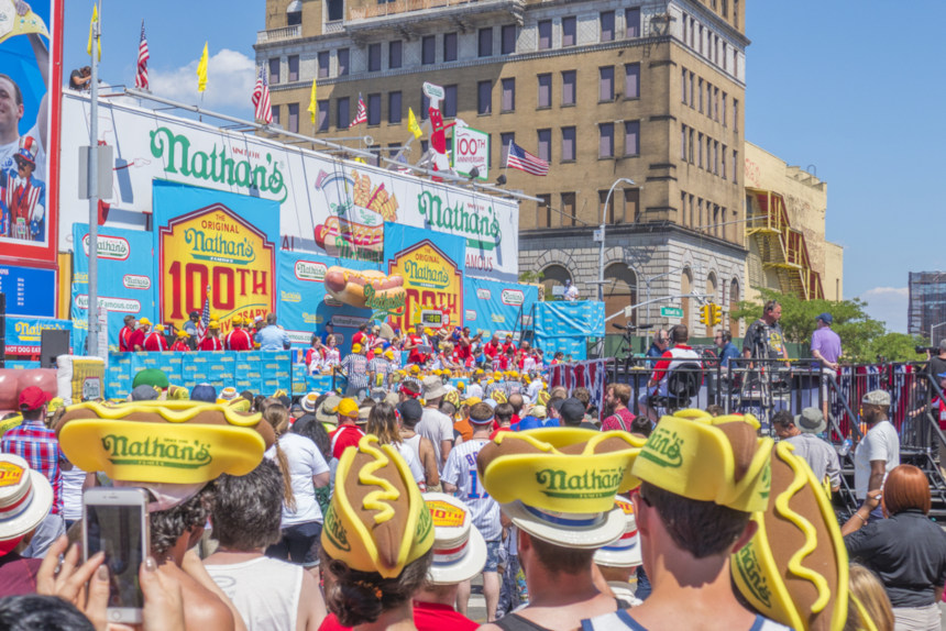 Crowd watches the Coney Island Hot Dog Eating Contest. Many in the audience are wearing hot dog-shaped hats.