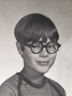Gay Haubner's school photo, showing her with thick-rimmed glasses and a bowl haircut.