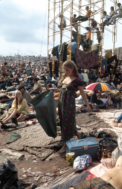 Woman walks through the crowd, picking up trash during the original Woodstock music festival in 1969.