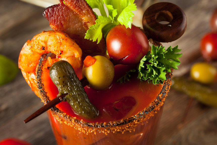 A glass of Bloody Mary, with shrimp, bacon, tomato, and olives.