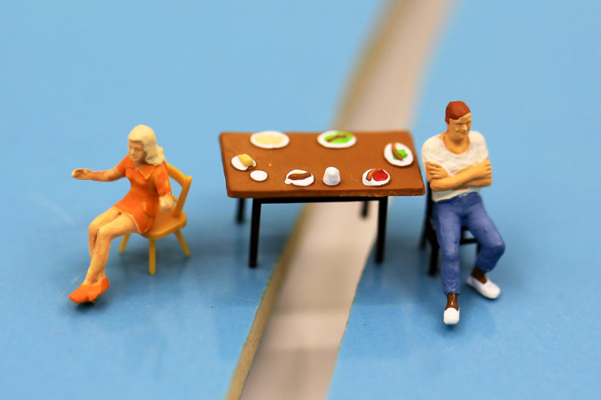 Miniature figures of a couple having an argument at a dinner table.