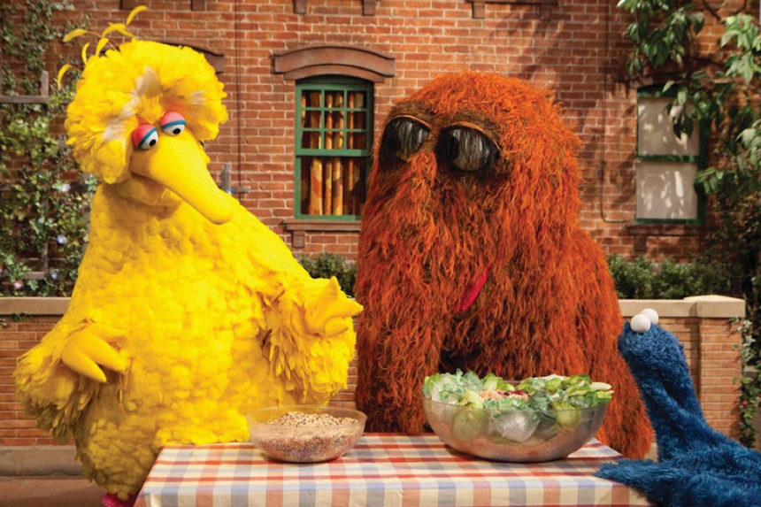 Big Bird and his friends, Snuffleupagus and the Cookie Monster, at a picnic table discussing the health benefits of vegetables.