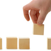 A row of wooden blocks, and a human hand lifting one of them off the ground.