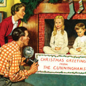 A father and mother takes a Christmas photograph of their children. Their son shows his displeasure as sits next to his patient sister.