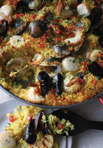 A pan filled with rice, shellfish, scallops, and tomatoes